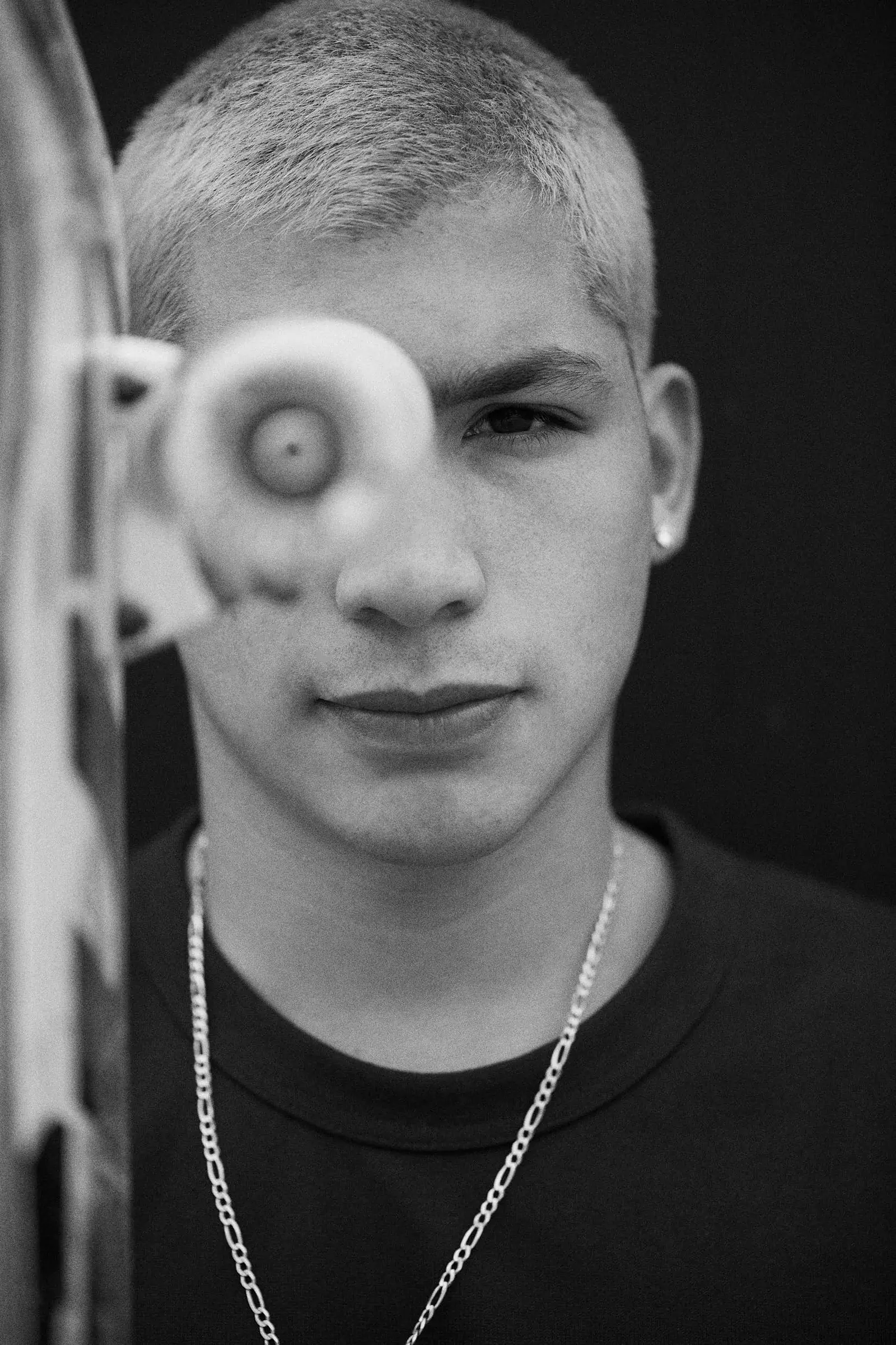 Portrait of skater Angelo Caro holding a skateboard wheel to his face, by Javier Falcón